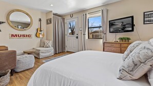 Une chambre avec un grand lit, une télévision, une guitare et un miroir au mur.