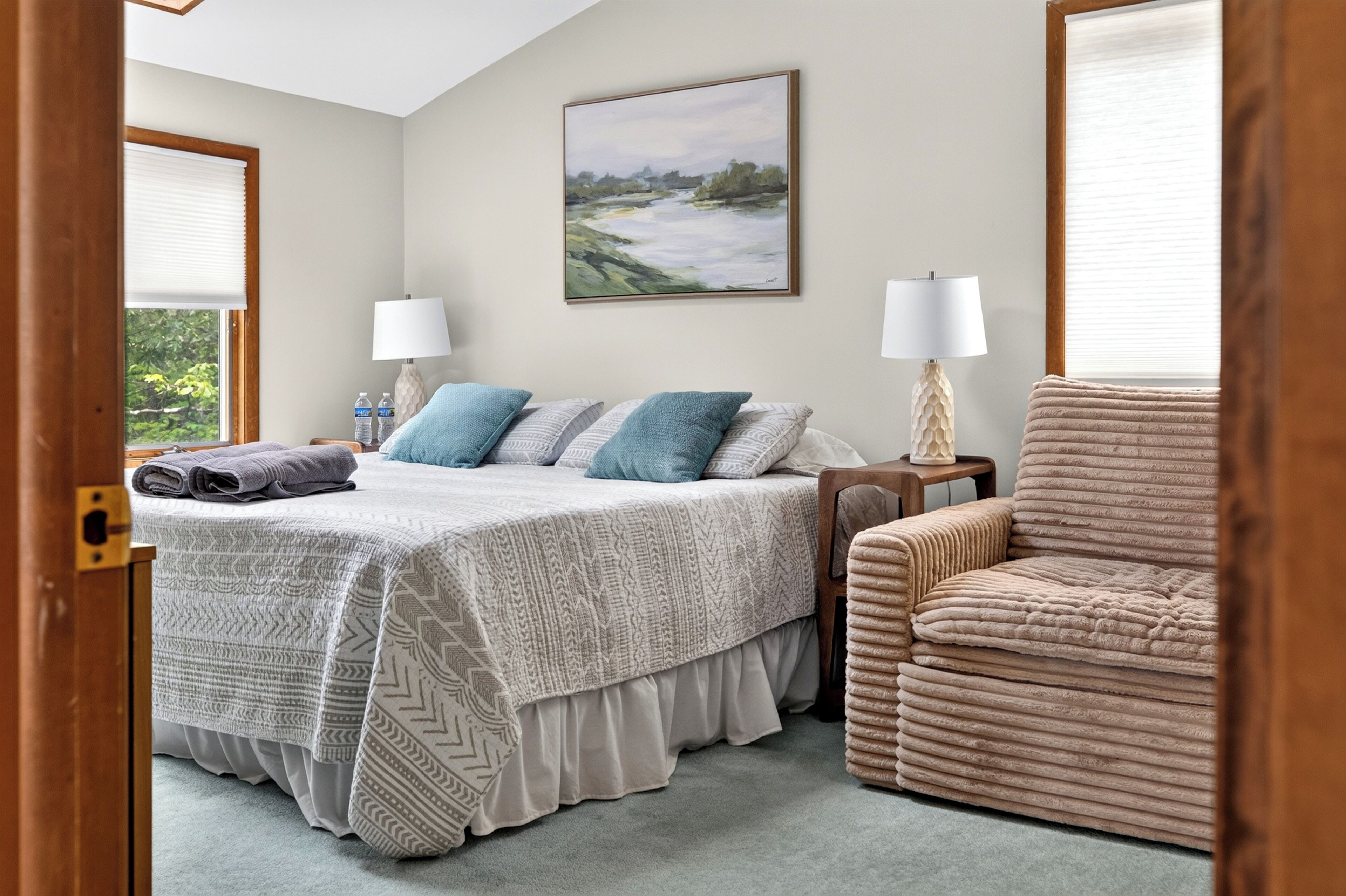 Quarto com cama, duas mesas de cabeceira, uma cadeira, um quadro e uma janela com persianas.