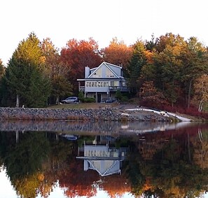 A lakeside house with a reflection in the water, surrounded by autumn-colored trees. - Lakefront Sunsets. Private Beach. Kayak, Fire Pit, Fish. near Camelback/Kalahari (Long Pond)