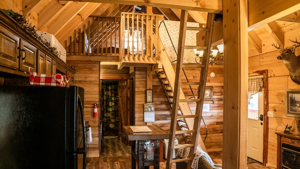 A wooden cabin interior with a kitchen, a dining area, a staircase, and a mounted deer head. - NEW! Custom Cabin on 10 acres! (Sevierville)