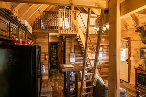 L’intérieur d’un chalet en bois comprend une cuisine, un coin repas, un escalier et une tête de cerf fixée au mur.