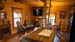A cozy cabin interior with a wooden dining table, two armchairs, a fireplace, and a television mounted on the wall. - NEW! Custom Cabin on 10 acres! (Sevierville)