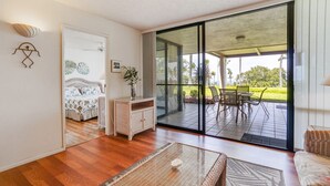 Ein modernes Wohnzimmer mit einem Glastisch, Korbmöbeln und Blick auf eine Terrasse mit Sitzgelegenheiten.