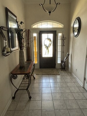 Enter a beautifully appointed hallway with a bench, chandelier, and mirror.