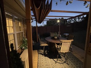 Un espacio de patio cubierto con una mesa redonda y sillas, una planta en maceta y una valla de madera al fondo.