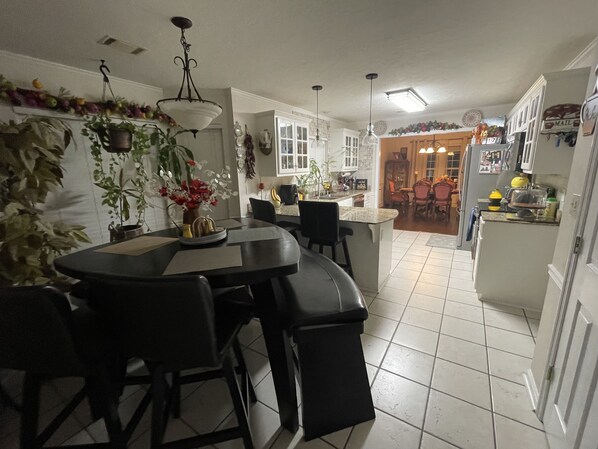 A kitchen with a dining area, featuring a central island, black chairs, and a hanging light fixture.