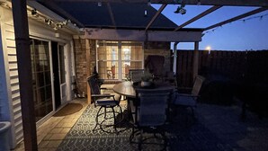 En uteplats med ett takförsett sittområde, ett bord och stolar.