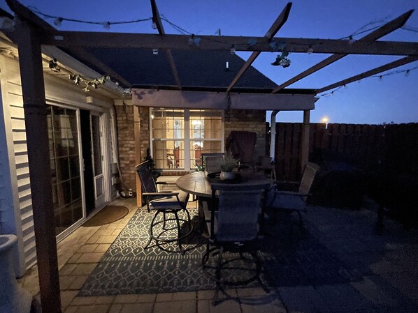 Relax outdoors with a round table and four chairs, surrounded by lush greenery and an entrance.