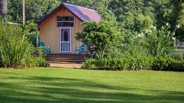 A small, single-story wooden cabin with a red roof, a front porch, and a white door.