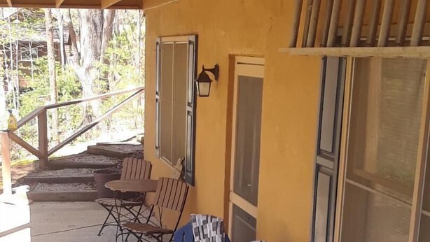 Un bain à remous avec deux chaises bleues, une terrasse en bois et un bâtiment jaune doté de fenêtres.