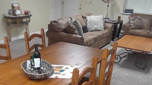 Un coin repas avec une table et des chaises en bois, un panier contenant des verres à vin et un mur décoré d’autocollants représentant des hiboux.