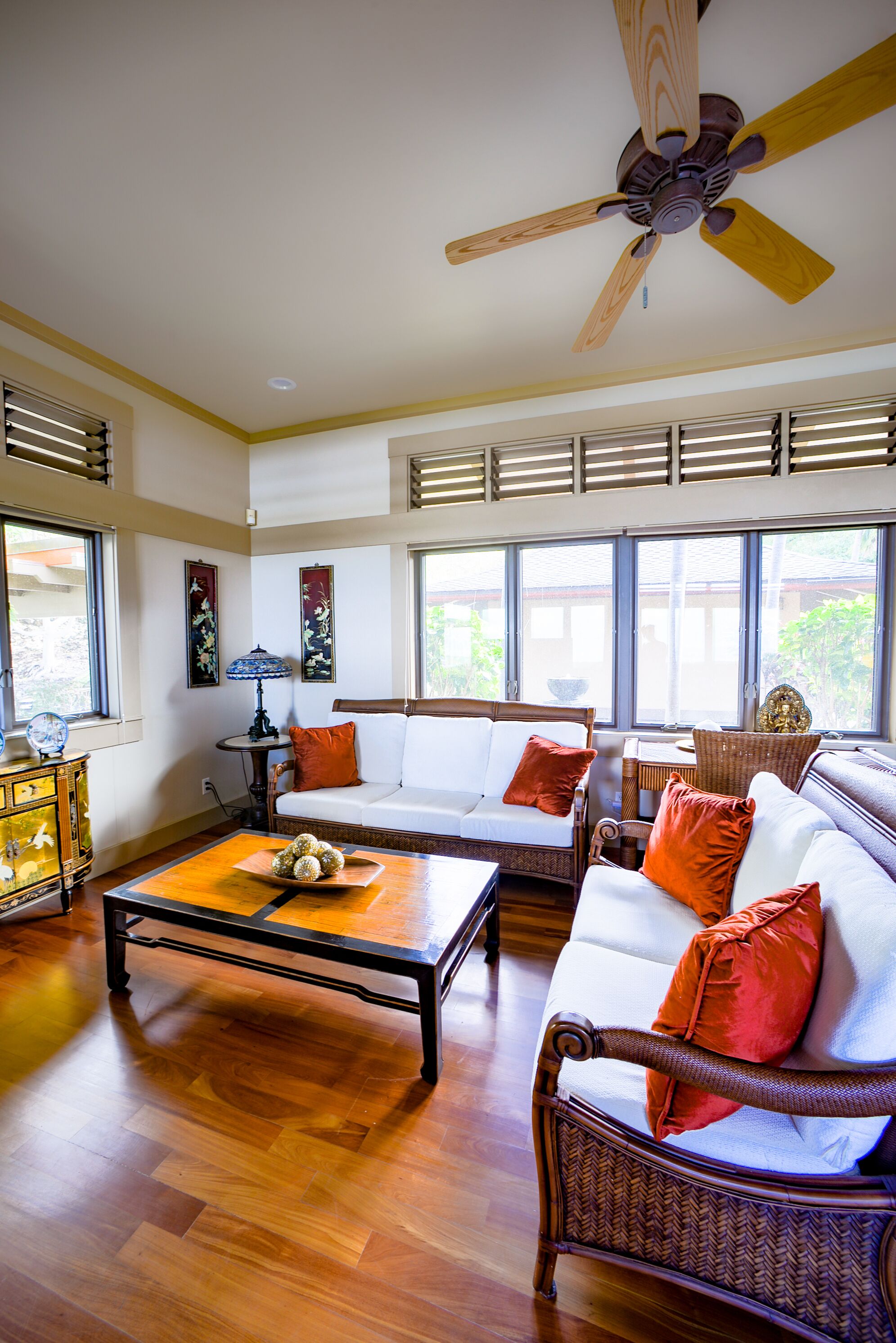 A spacious living room with a wooden floor, a ceiling fan, and large windows.