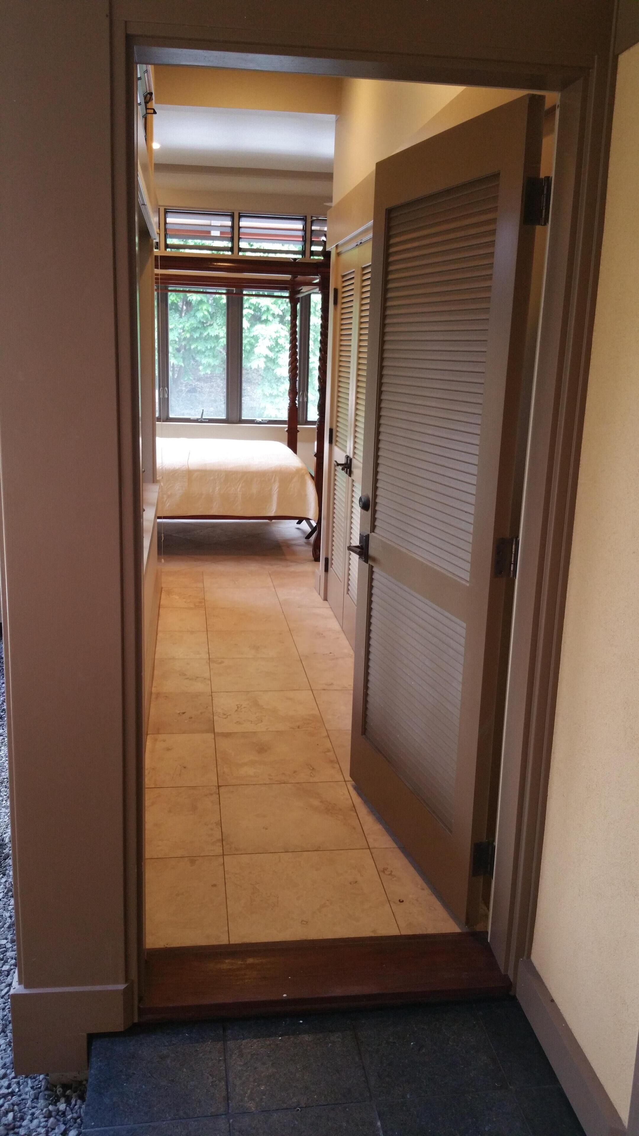A narrow hallway leading to a bedroom with a bed, a window, and a door with a screen.