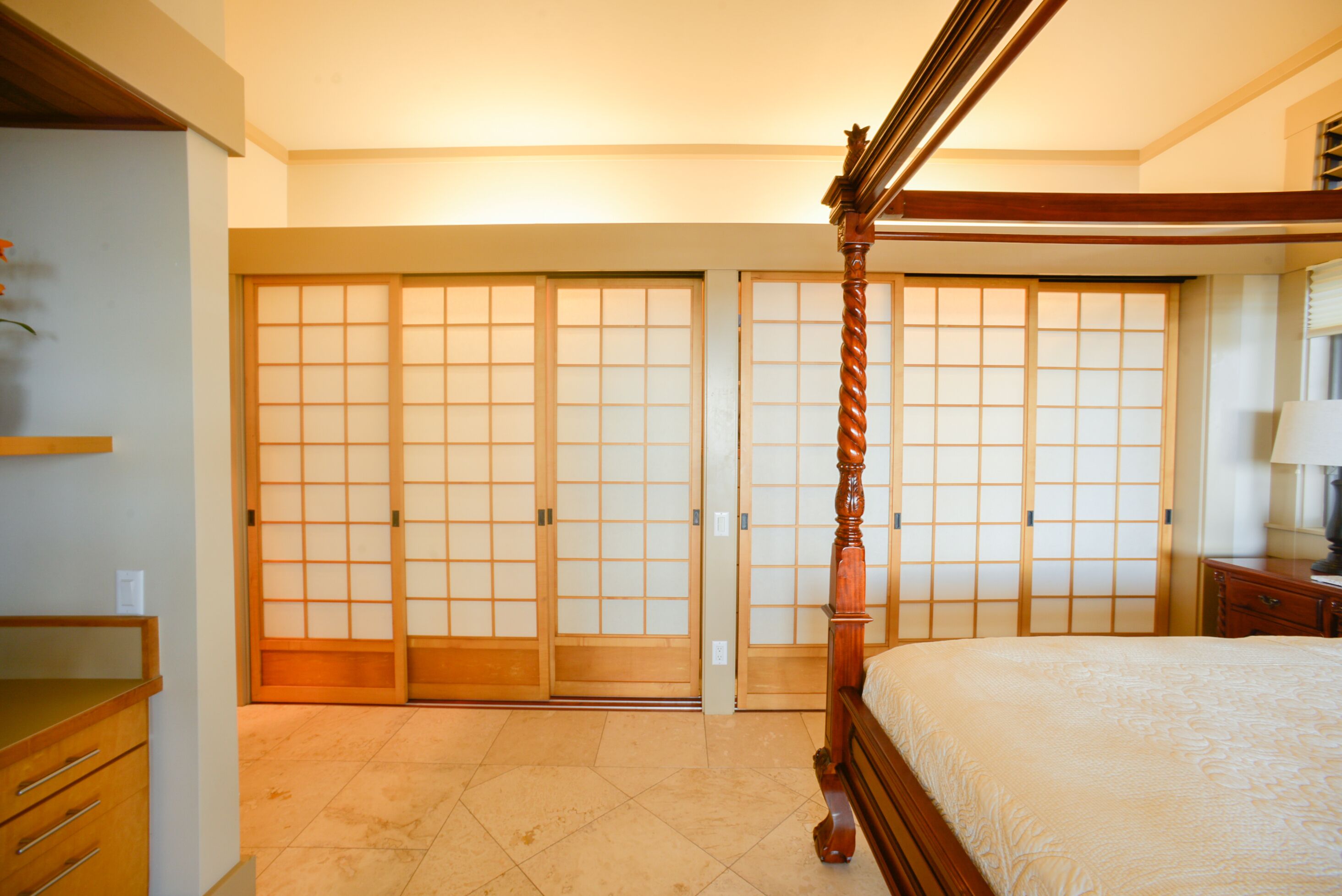 A bedroom with a four-poster bed, sliding shoji doors, and a wooden dresser.