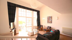 Una sala de estar amplia con un gran ventanal corredera que da a un espacio exterior, un sofá, dos sillones, una mesa de centro y un televisor.