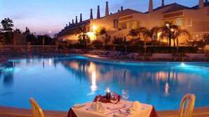 Zona de comedor junto a la piscina con una mesa lista para dos, con vista a la alberca.
