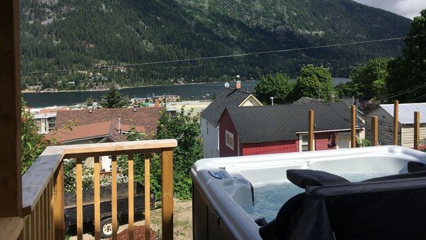 Uma banheira de hidromassagem em um deck com vista para um lago e montanhas ao fundo.