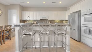 A kitchen with white cabinets, stainless steel appliances, and a central island with bar stools. - An Elegant Palm Desert Home, Great Nightly Rate! (Palm Desert)