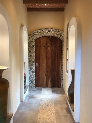 A hallway with a stone archway leading to a wooden door, a concrete floor, and white walls. - Beautiful vacation home with ocean views nestled in the jungle with a pool (Chacala)