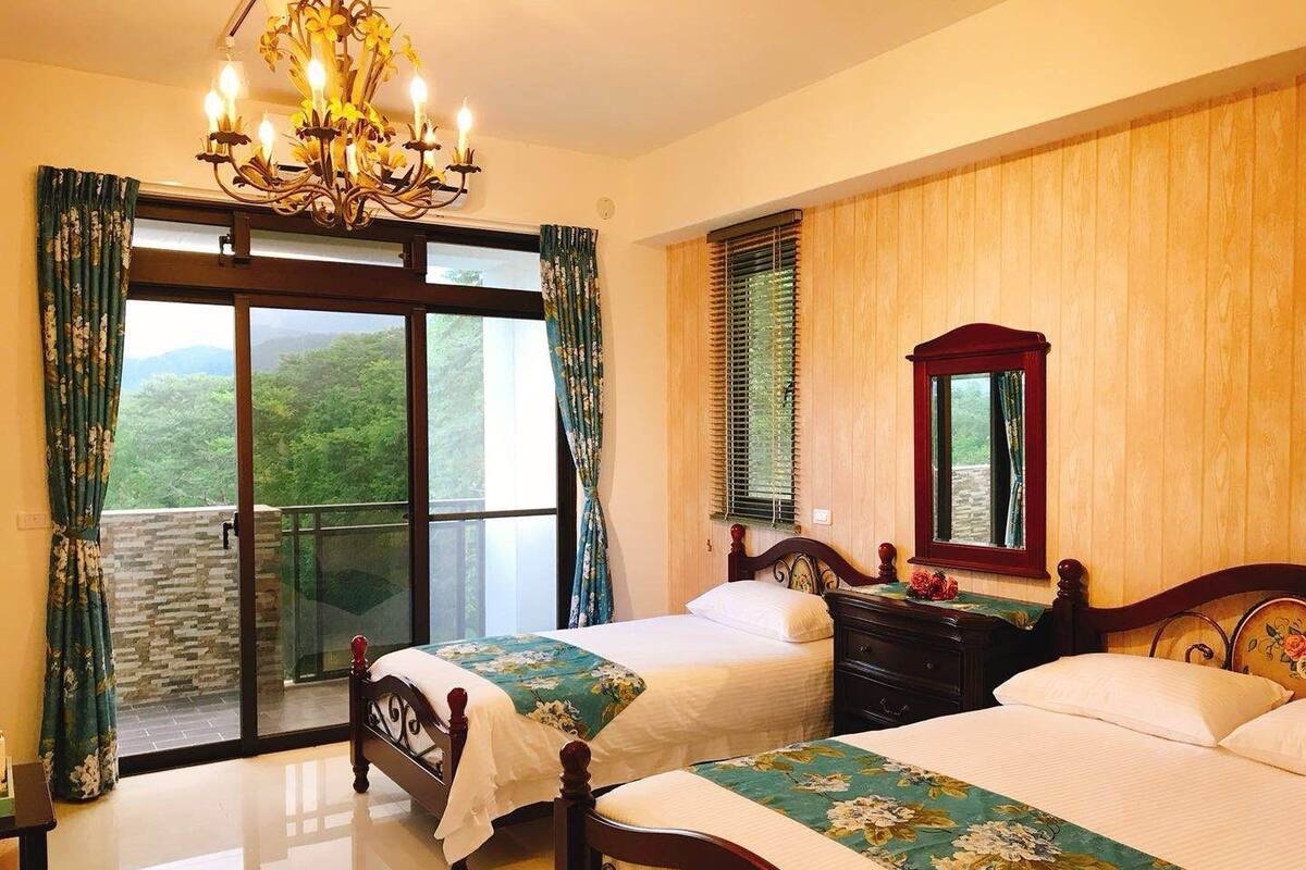 A bedroom with two beds, a chandelier, a wooden dresser, and a window with blinds.