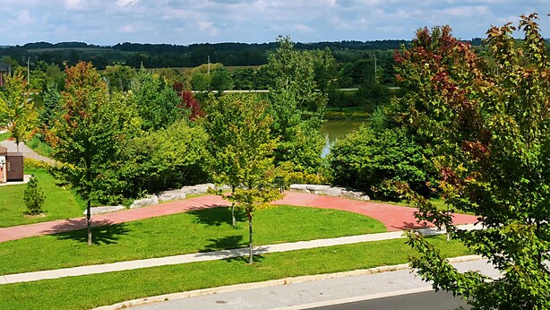 A park with a paved walkway, trees, and a body of water in the background. - Entire 3 Bedroom Townhouse in Markham (Markham)