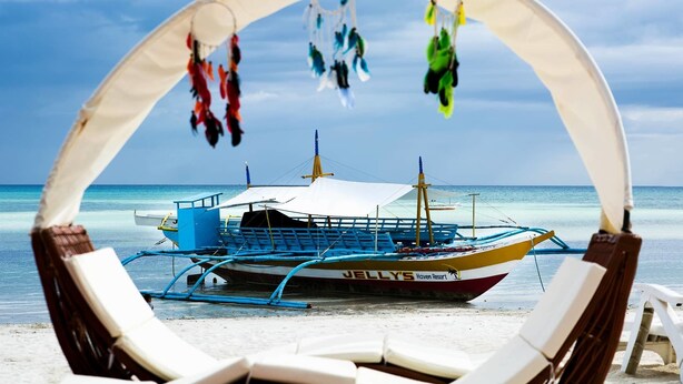 A beach with a boat named 'JELLY'S Haven Resort' anchored near the shore, surrounded by lounge chairs. - Jelly's Haven Resort (Santa Fe)