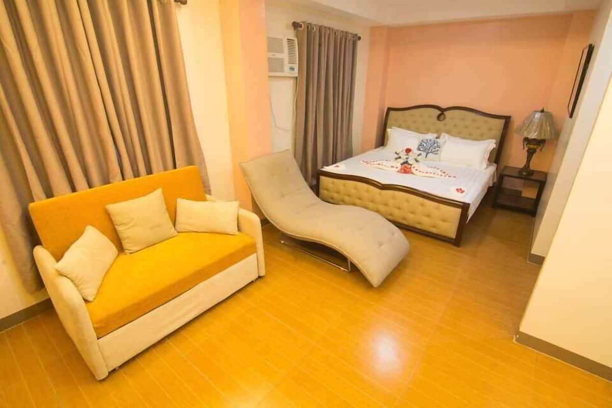 A hotel room with a bed, a sofa, a chair, and a lamp.