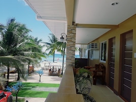 Un balcón con vista a la playa, palmeras y mobiliario exterior.