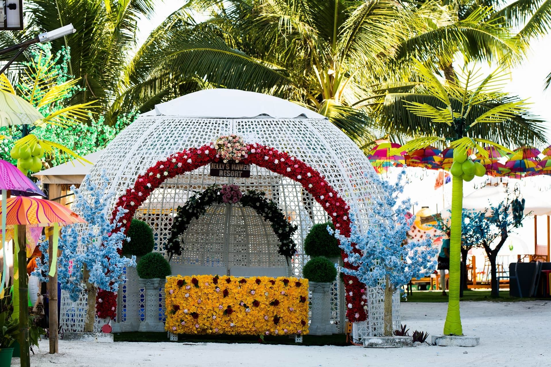 Een decoratieve boog versierd met bloemarrangementen en een bord met de tekst 'Jelly's Navel Resort'.