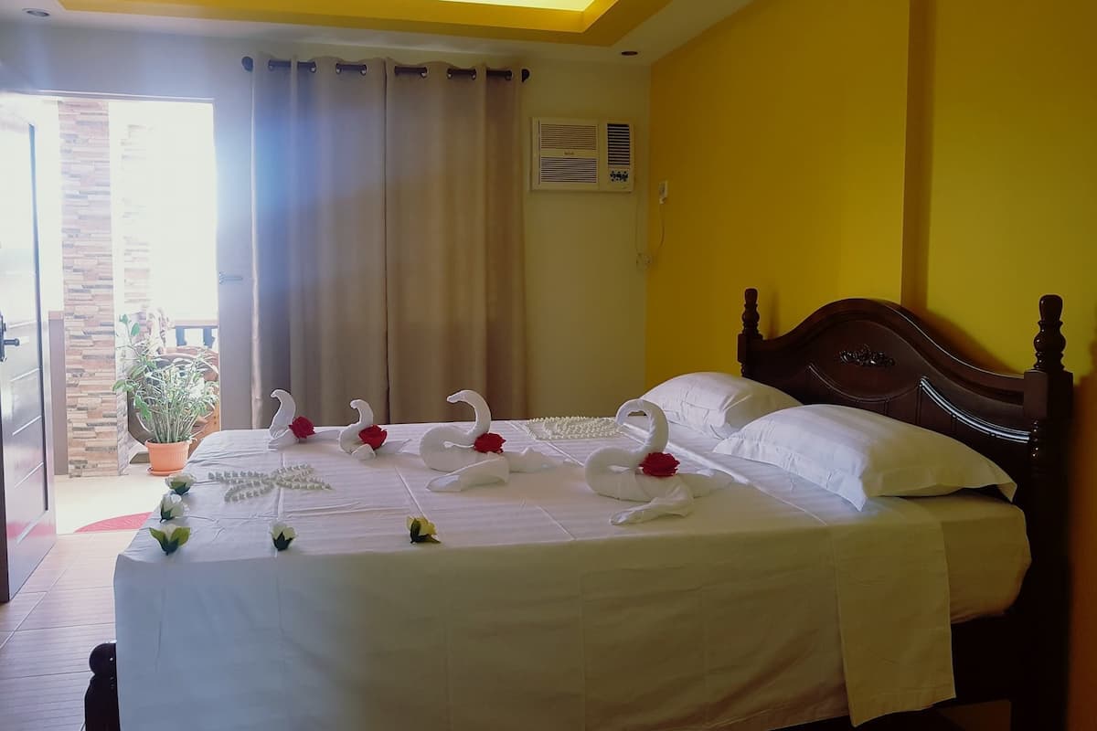 A hotel room with a bed, a potted plant, and a view of the outside.