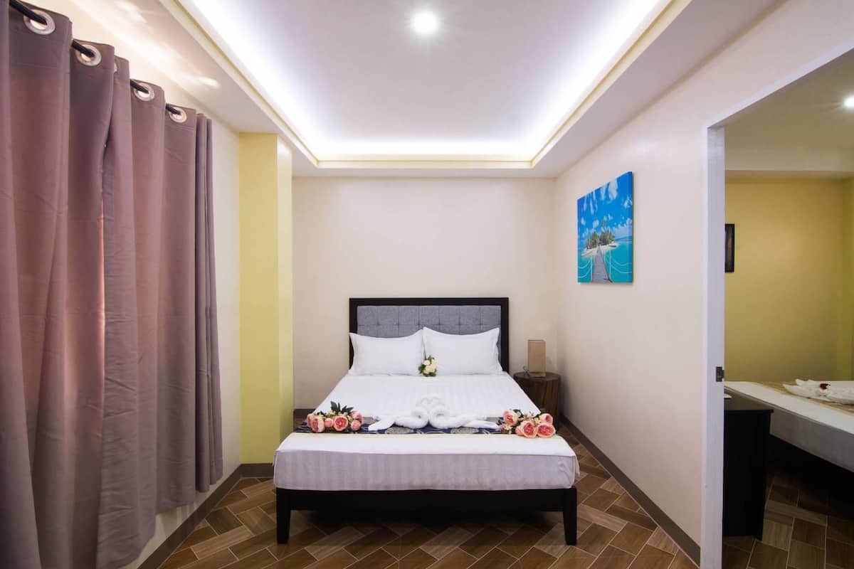 A neatly arranged hotel room with a bed, a bedside table, a nightstand, a painting on the wall, and a bathroom visible through an open door.
