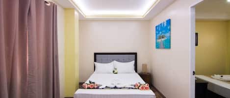 A neatly arranged hotel room with a bed, a bedside table, a nightstand, a painting on the wall, and a bathroom visible through an open door.