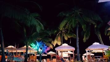 A nighttime outdoor seating area with palm trees and umbrellas.