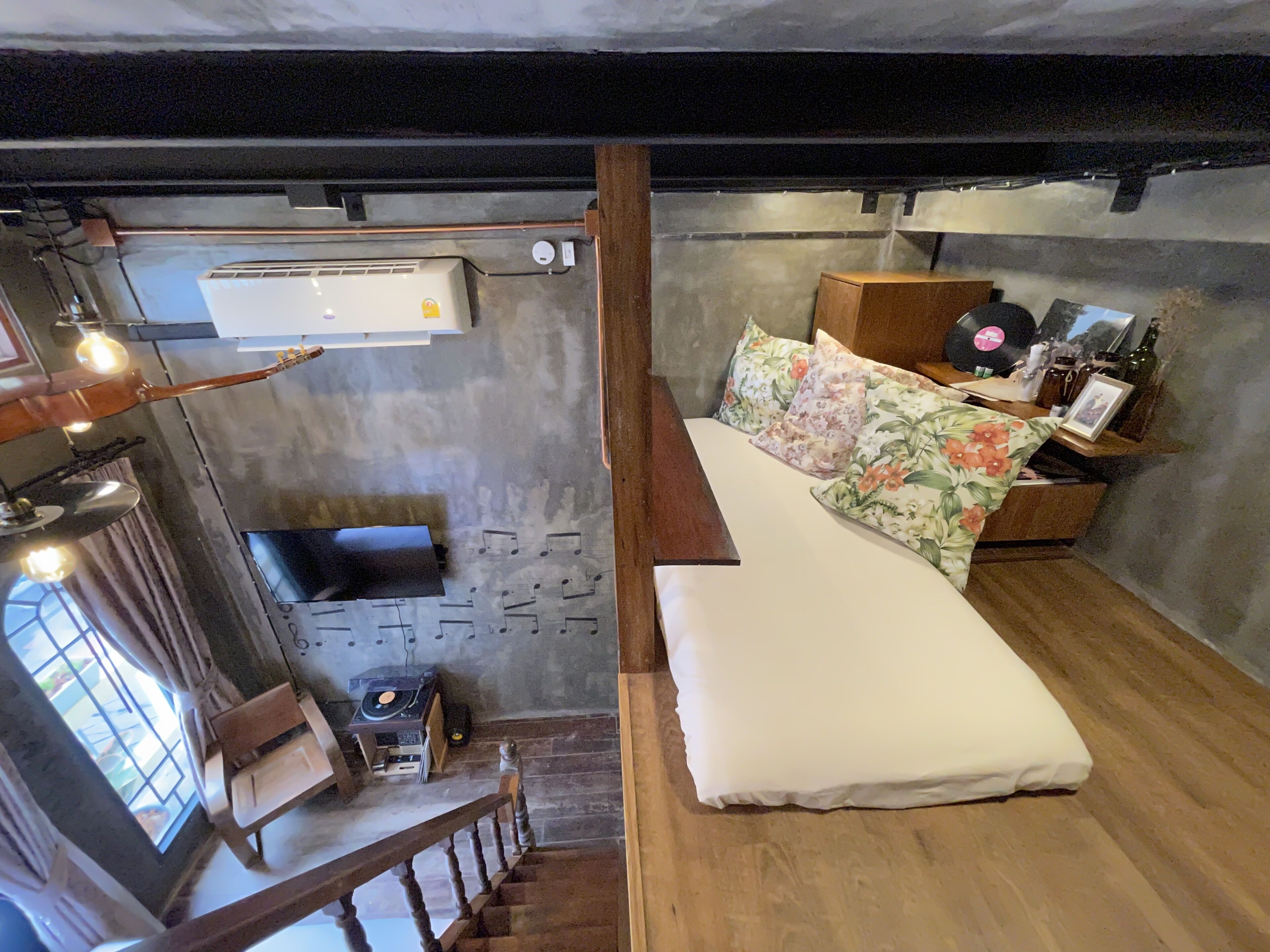 A cozy room with a wooden staircase, a bed with floral bedding, a small table with a record player, and a window with curtains.