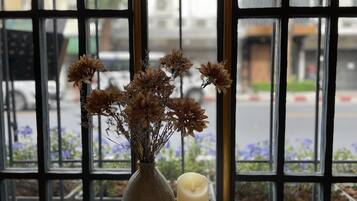 A vase with dried flowers and a candle on a table by a window with a view of the street.