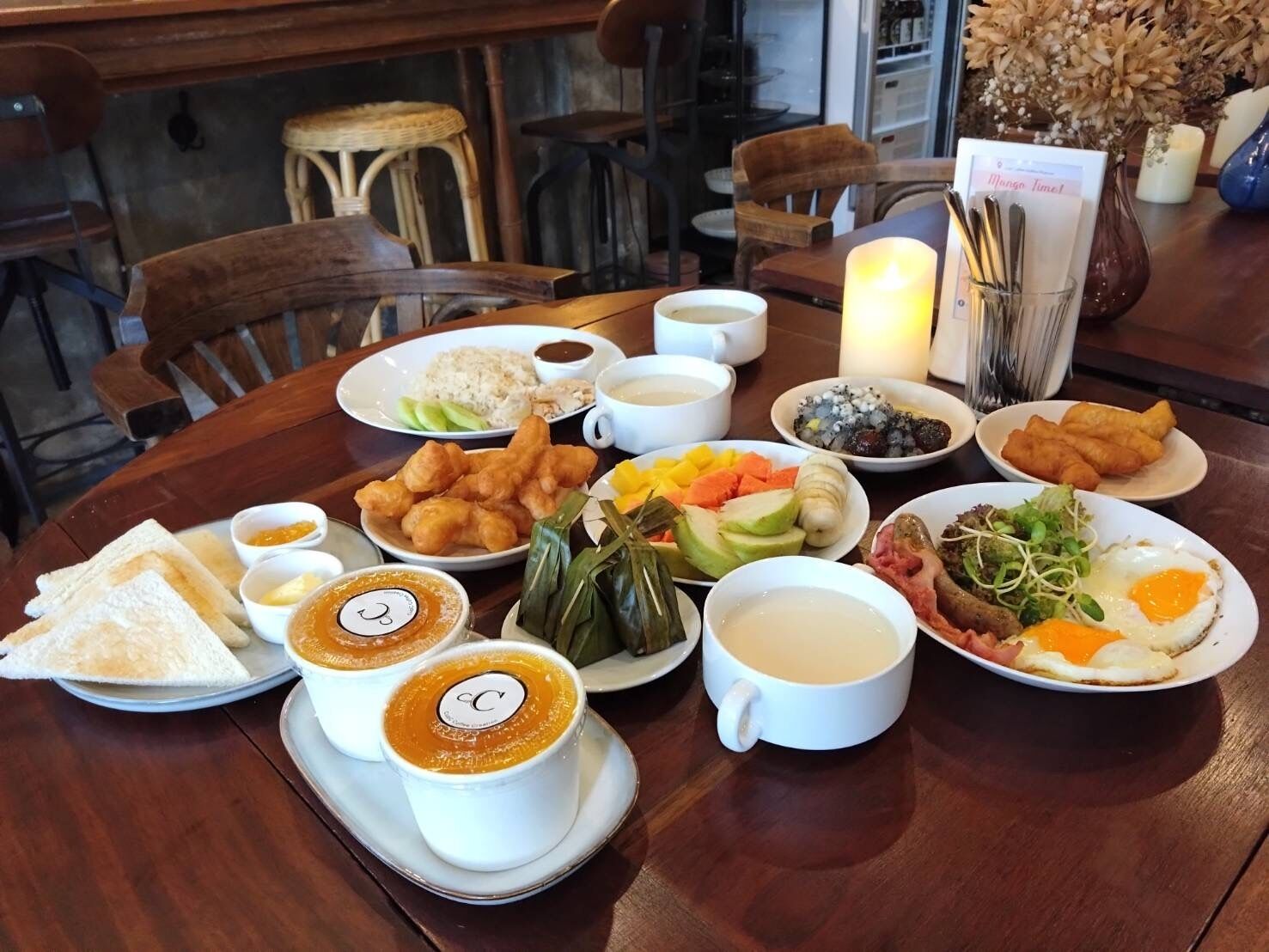 A table set with a variety of dishes including rice, fried items, fresh vegetables, and a cup of coffee.