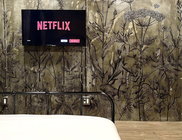 A room with a bed, a wall-mounted TV displaying 'NETFLIX', and a floral wallpaper design. - Central Old Town Cottage (Bangkok)