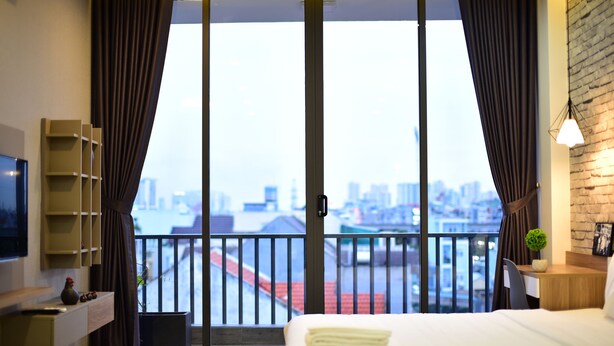 A hotel room with a bed, a desk, a TV, and a balcony with a city view. - Karta Riverview Apartment (Ho Chi Minh City)