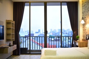 A hotel room with a bed, a desk, a TV, and a balcony with a city view. - Karta Riverview Apartment (Ho Chi Minh City)