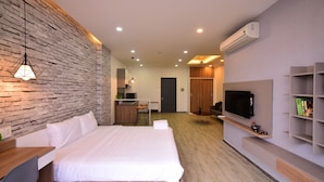 A modern hotel room with a large bed, a desk with a chair, a TV mounted on the wall, and a small kitchenette area. - Karta Riverview Apartment (Ho Chi Minh City)