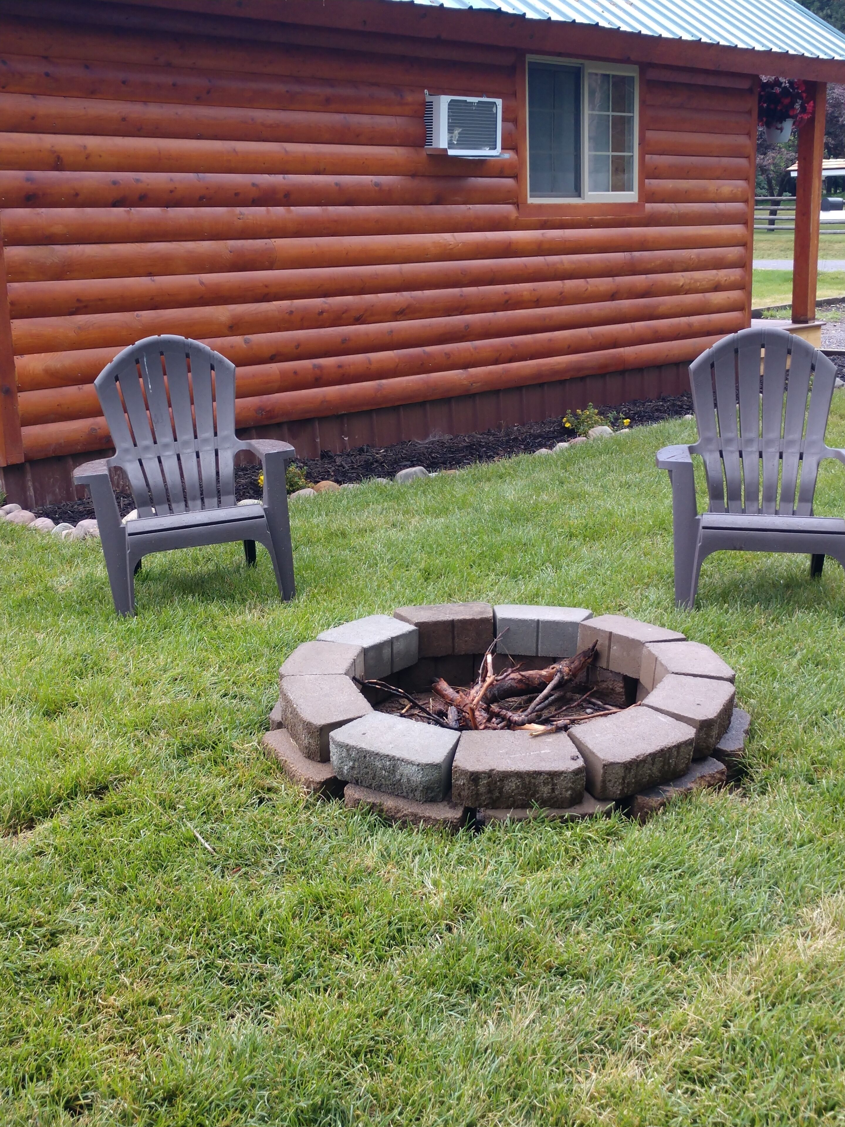 A log cabin with two Adirondack chairs and a fire pit in the yard.