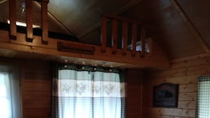 Un interior de cabaña acogedor con una mesa de comedor de madera, dos sillas, un sofá y una escalera que lleva a un nivel superior.