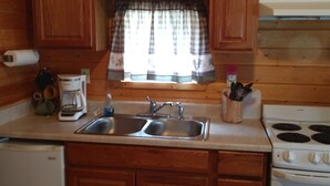 Una cocina compacta con armarios de madera, un lavamanos empotrado, una estufa y una ventana con cortina a cuadros.