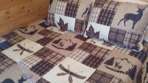 Habitación de cabaña de madera con cama cubierta por un edredón escocés con diseño de ciervos y hojas.