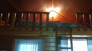 Un interior de madera con una escalera, una ventana con cortinas y una lámpara.