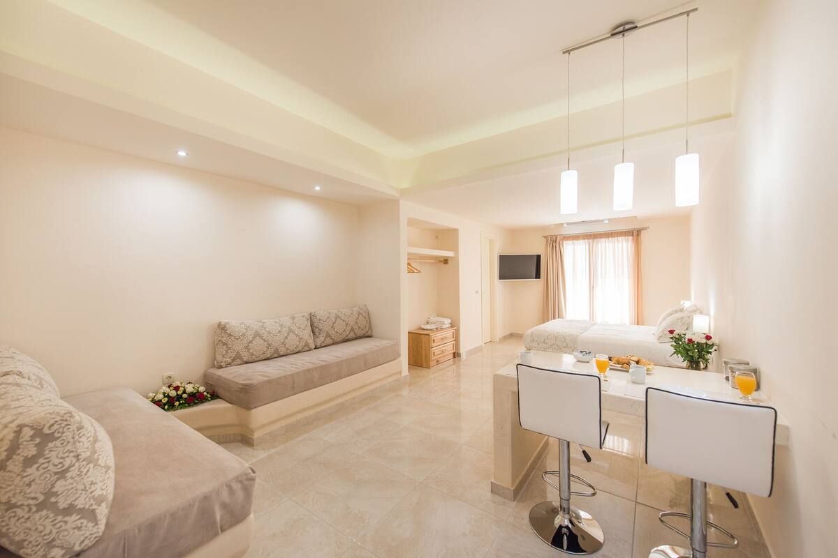 A spacious hotel room with a large bed, a sitting area with a sofa, a small desk with a chair, and a television.