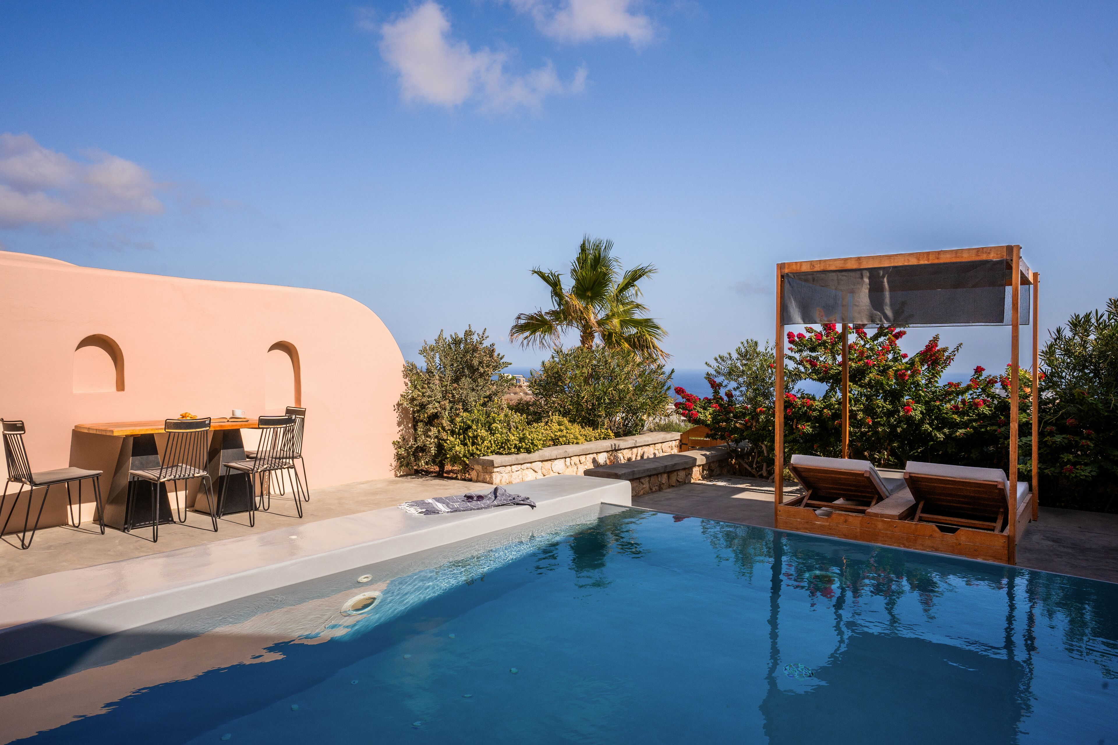 A pool area with a lounge chair, a table with chairs, and a pergola with a screen.