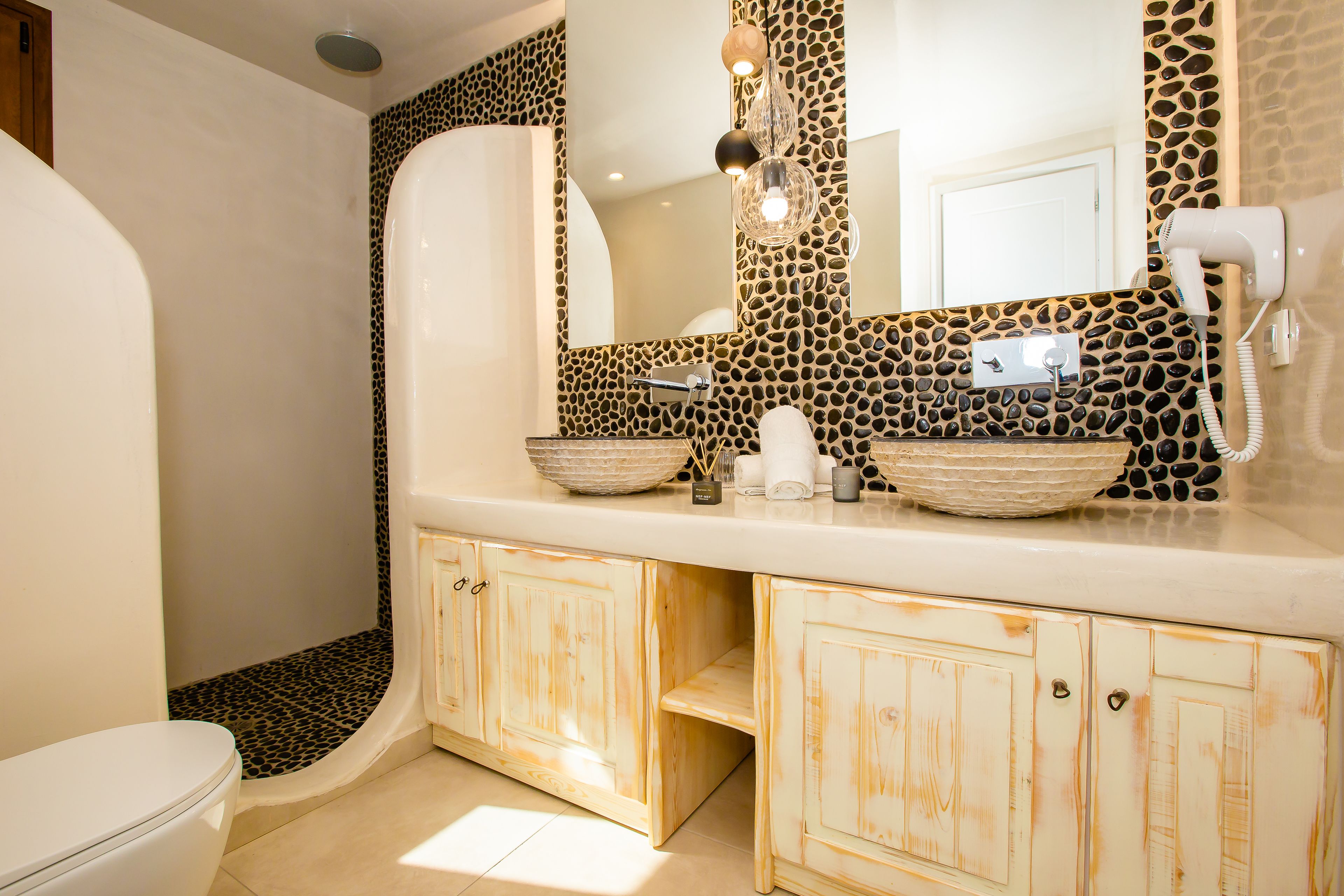 A bathroom with a white toilet, a vanity with a mirror, and a hairdryer on the wall.