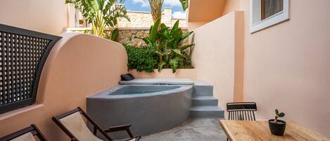 A small outdoor area with a hot tub, wooden chairs, a table, and potted plants.
