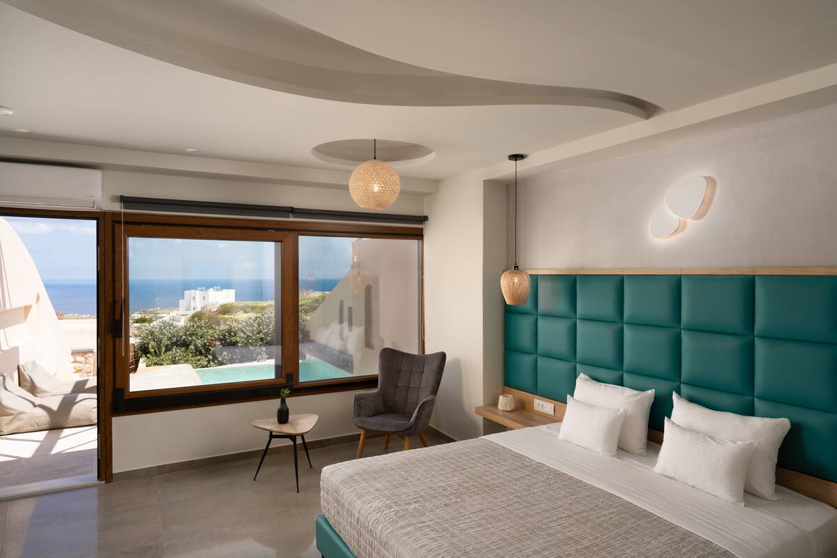 A modern bedroom with a large bed, a view of the sea, and a comfortable chair.